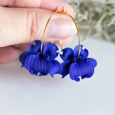 a person is holding two blue flowers in their hand and they are wearing gold hoop earrings