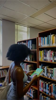 a woman standing in front of a book shelf filled with books and holding a book