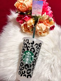 the starbucks cup has been decorated with leopard print and is next to pink flowers on a fluffy white rug