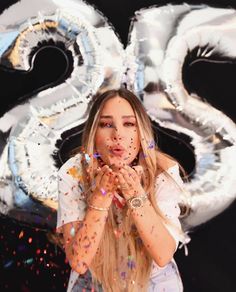 a woman standing in front of a number 20 sign with confetti on her hands