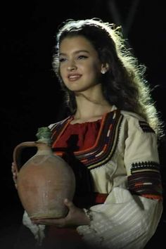 a woman is holding a large vase in her right hand and smiling at the camera