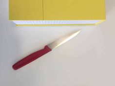 a knife sitting on top of a yellow piece of paper next to a red object