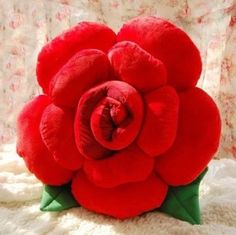 a large red flower sitting on top of a white fur covered bed next to a window