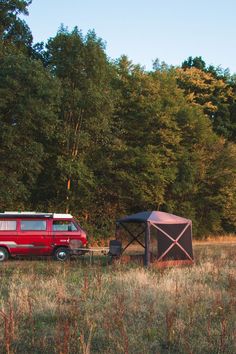 a red van parked next to a tent in the middle of a grass covered field