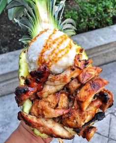 someone holding up a pineapple with chicken and rice on it