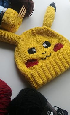 a knitted pikachu hat sitting on top of a table next to yarn balls