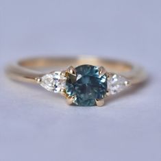 Unique engagement ring with 1 ct Montana Sapphire and Natural Diamonds. This nature inspired floral design engagements ring features gorgeous teal green Montana sapphire, ethically sourced directly from the Rock Creek Montana mine. Its floral design makes the sapphire engagement ring so delicate and sophisticated. Montana Sapphire Engagement Rings have become increasingly popular. A lot of people have their own stories, connected with Montana State and they want to have a piece of it with them f Teal Montana Sapphire Engagement Ring, Floral Design Engagement Ring, Engagements Ring, Gold Three Stone Engagement Ring, Sparkly Rings, Blue Green Sapphire Ring, Montana Sapphire Engagement, Montana Sapphire Engagement Ring, Green Montana