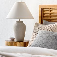 a white lamp sitting on top of a bed next to a wooden headboard and night stand