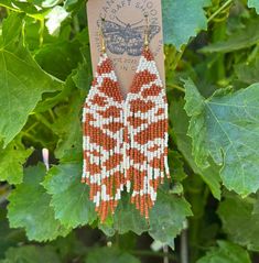 an orange and white beaded earring hanging from a leafy plant with green leaves