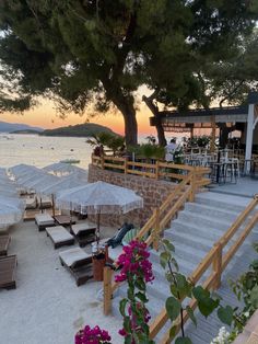 people are sitting under umbrellas on the beach by the water at sunset or dawn