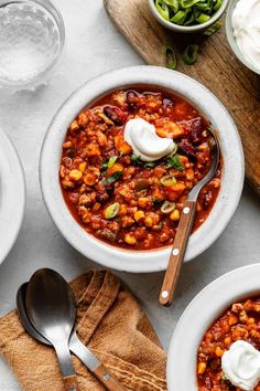 two bowls of chili with sour cream on the top and spoons next to them