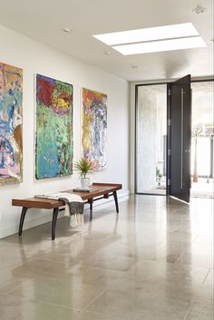 three paintings hang on the wall next to two benches in a large room with tile flooring