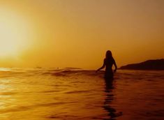 a woman standing in the ocean at sunset