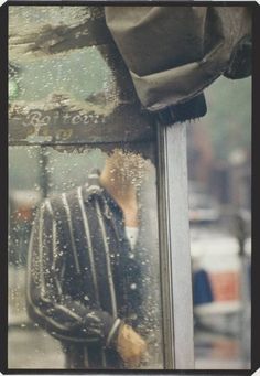 a man standing next to a window covered in rain