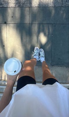 a person sitting on the ground with their feet up and holding a paper cup in front of them