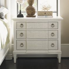 a white dresser sitting next to a bed in a room with a lamp on top of it