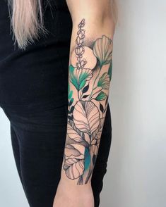 a woman's arm with flowers and leaves tattooed on her left arm, while she is wearing a black top