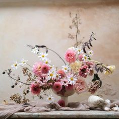 a vase filled with pink and white flowers on top of a wooden table next to shells