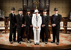 a group of men standing on top of a stage wearing black and white suits with hats