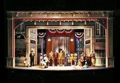 an outdoor stage set with people dressed in costumes and onlookers standing around