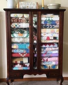 an armoire with many quilts on it and a vase sitting on top of it