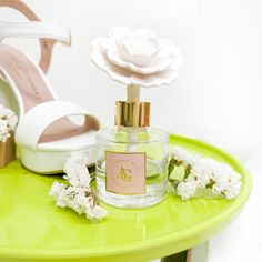 a green table topped with white flowers next to a bottle of perfume on top of it