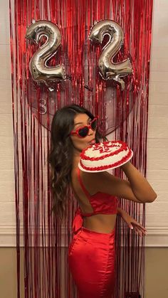 a woman in a red dress holding a cake with the number twenty two on it