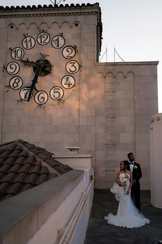 a bride and groom standing in front of a large clock on the side of a building