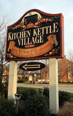 the sign for kitchen kettle village is in front of some bushes and trees with houses behind it