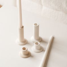 three white candles on a table with one candle holder and the other two are empty