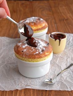 two desserts with chocolate sauce on top and spoon in the bowl next to them