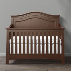 a brown crib with white sheets and pillows on the bottom bed, against a gray wall