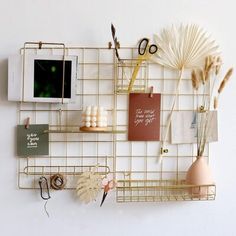 a white wall with gold wire shelves and various items on it, including a computer monitor