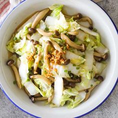 a white bowl filled with lettuce, mushrooms and other vegetables on top of a table