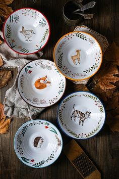 three bowls with animals painted on them are sitting on the ground next to leaves and scissors