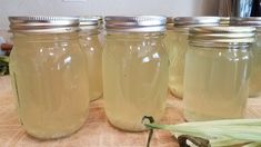 four jars filled with liquid sitting on top of a table next to an unpeeled plant