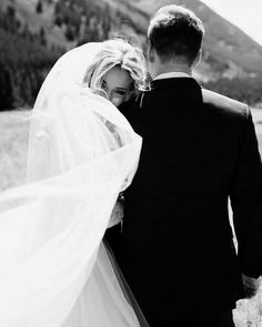 a bride and groom walking through the mountains in black and white, holding each other's arms