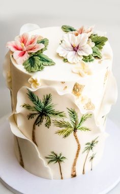 a cake decorated with palm trees and flowers on a white platter that is sitting on a table