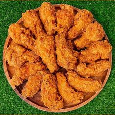 a wooden plate filled with fried chicken on top of green grass