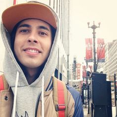 a man wearing a hat and backpack standing in front of a tall building on a city street