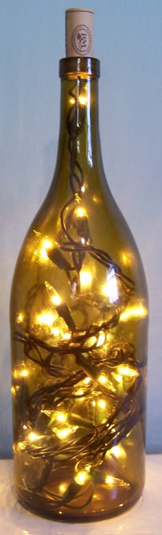 a bottle with some lights in it sitting on a table next to a vase filled with flowers