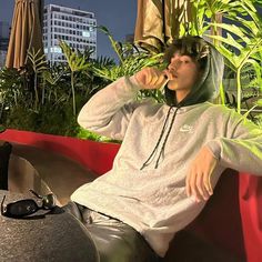 a young man sitting on a red bench drinking from a cup while wearing a hoodie