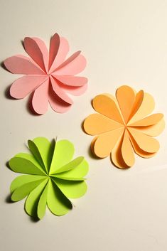 three different colored paper flowers on a white surface