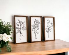 three framed flowers sit on a table next to a vase with white flowers in it