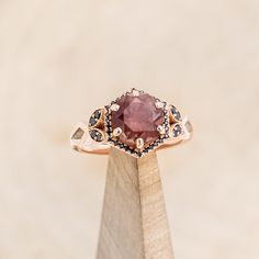 a close up of a ring on top of a wooden stand with a pink stone