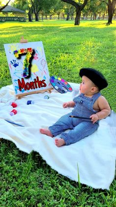 a baby sitting on a blanket in the grass next to a sign that says 1 months