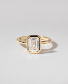 a gold ring with an emerald cut diamond in the center, on a white background