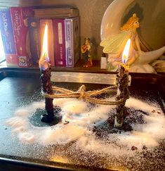 two candles sitting on top of a table covered in white powder next to a fairy figurine