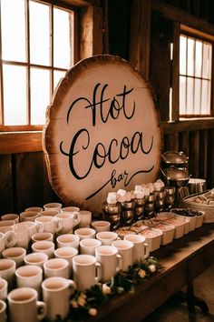 there is a sign that says hot cocoa at the table with many cups on it