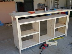 an unfinished entertainment center being built in a garage with tools on the floor next to it